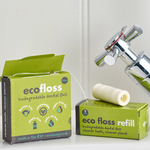 Eco-friendly dental floss packaging with a roll of floss next to it on a bathroom counter.